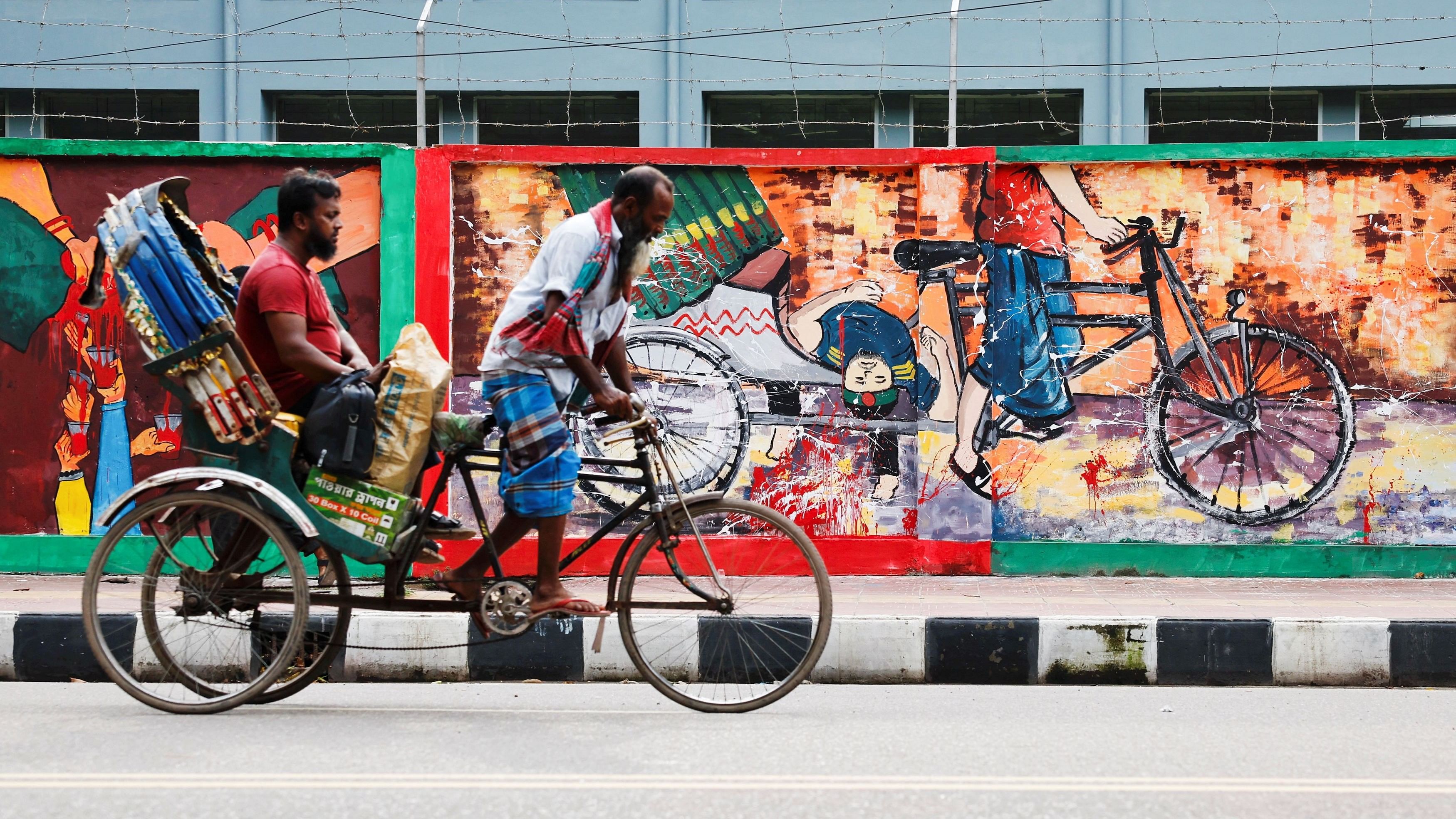 <div class="paragraphs"><p>A rickshaw passes by graffiti depicting a rickshaw carrying a student's body during a protest at the University of Dhaka area in Dhaka</p></div>